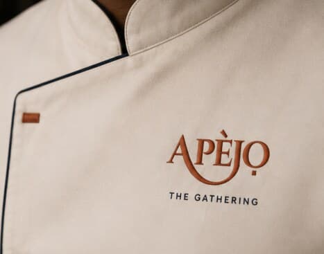 The Apèjọ wordmark embroidered on a chef's jacket